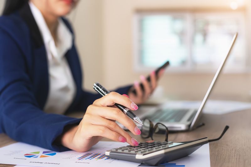 Female financial advisor writing on diary while sitting with laptop at desk in office