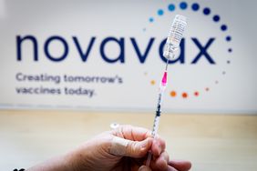  A close-up of a person's hand preparing a dose of a Novavax vaccine, with the company's logo in the background.