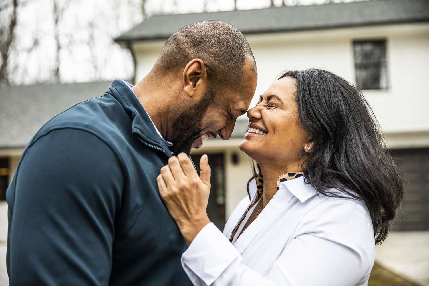 Married couple embracing in front of residential home whole life insurance