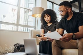 Woman and man looking a paperwork with a laptop on a couch