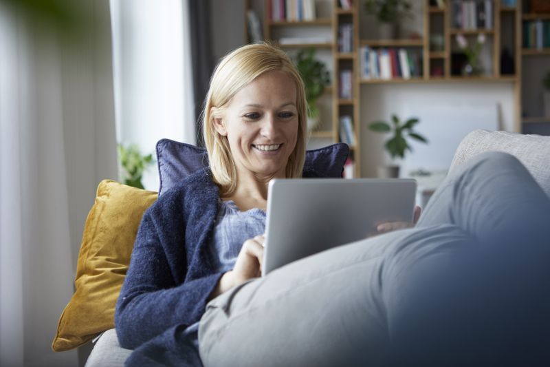 Woman in her 30s sitting on her couch and looking happily at something on her laptop
