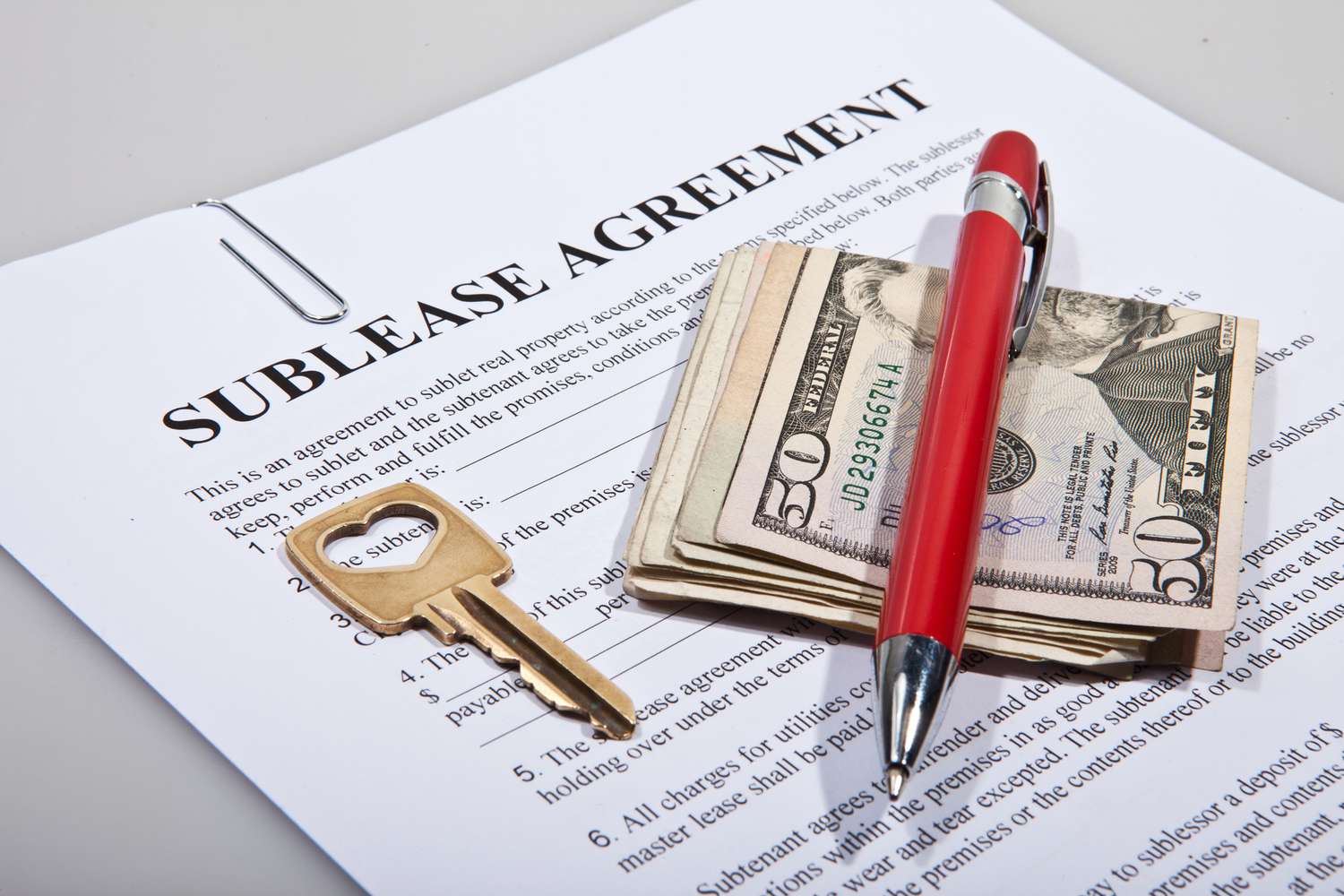 A sublease legal agreement with a key, pen and folded money