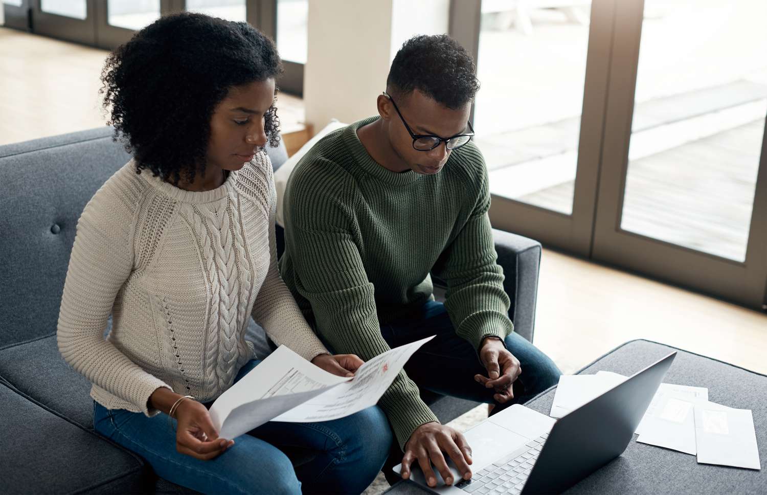 Young couple sitting on their sofa and looking at mortgage documents and a laptop