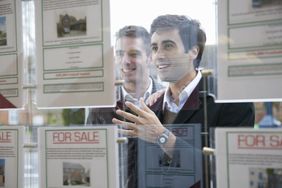 Two men looking at property listings in the window of a real estate agent's office