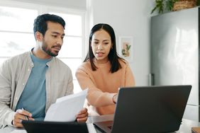 Young couple sitting in their kitchen and looking at mortgage documents and rates on a laptop