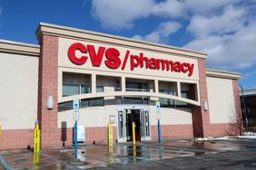 The exterior of a CVS Pharmacy is seen with a parking lot in front and cloudy blue sky behind.
