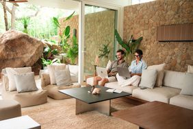 A couple works on their laptops while sitting next to each other on a couch inside of a luxury vacation home.