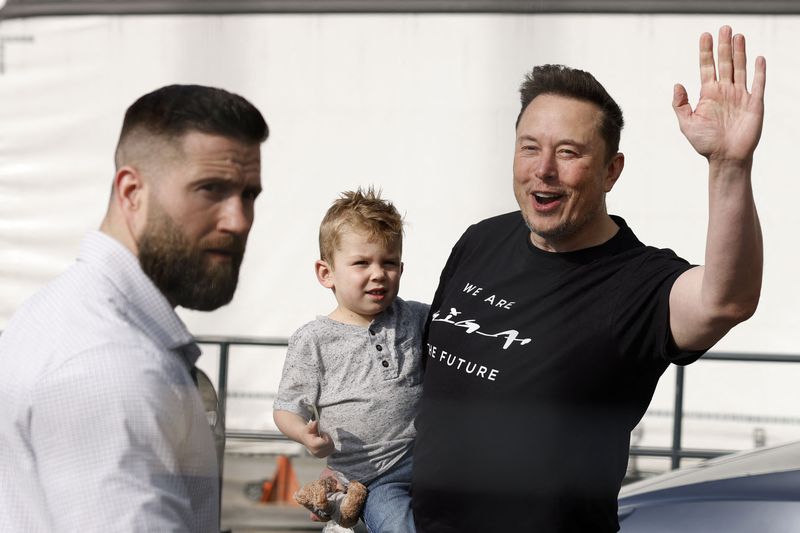 Elon Musk waving to fans while carrying his son.