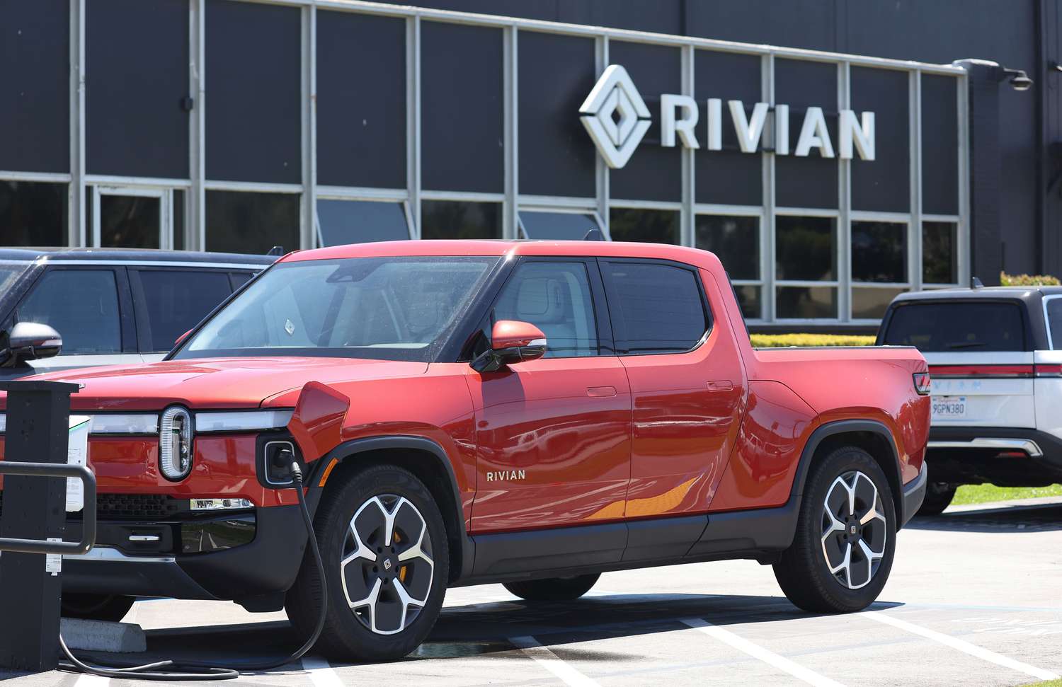 Red Rivian EV truck being recharged in front of a Rivian dealership