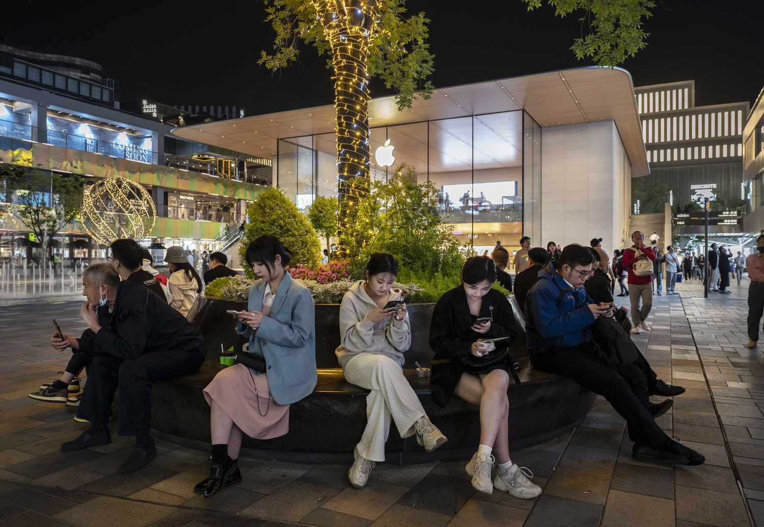 People sit on a bench outside an Apple Store in Beijing, China.