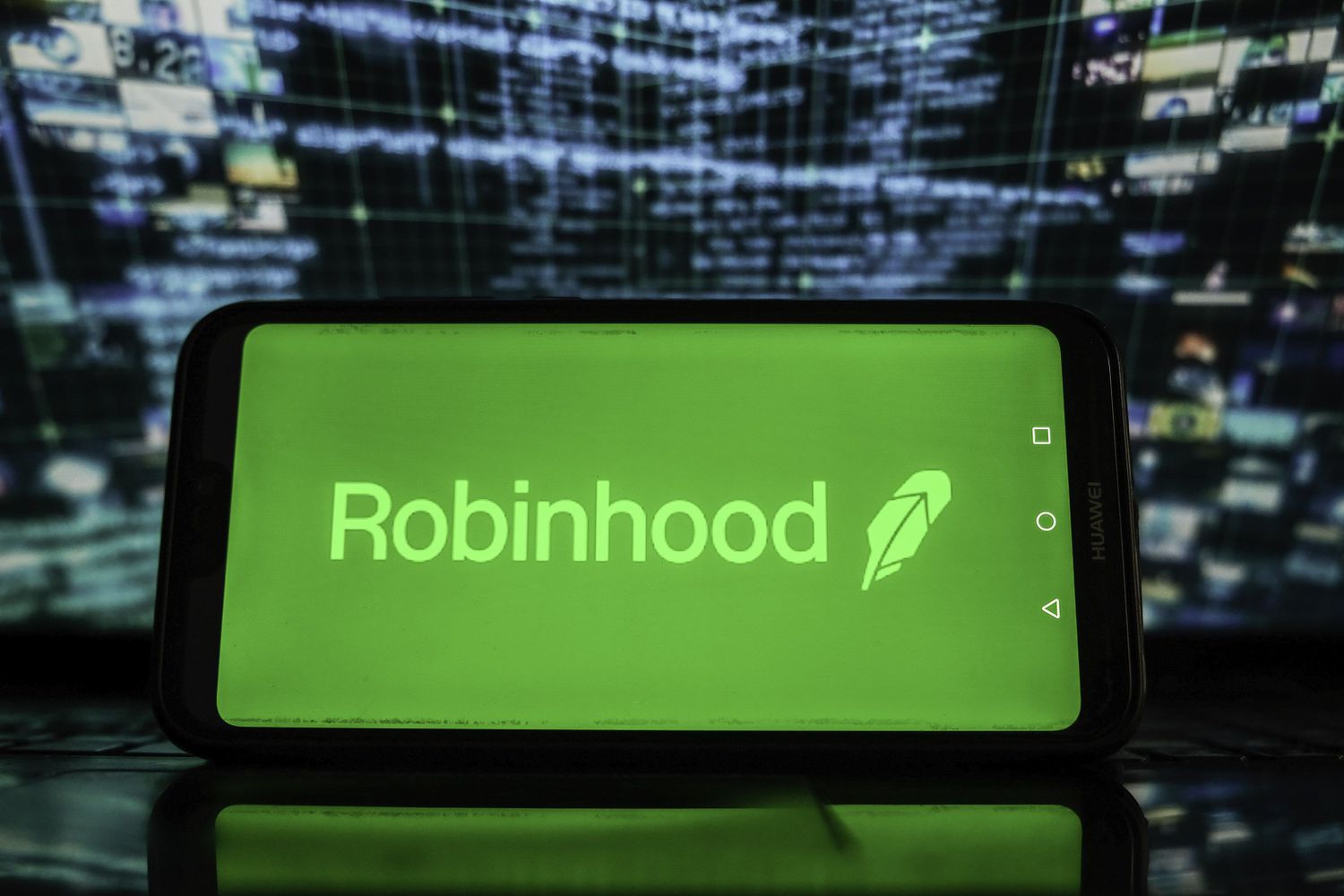Robinhood logo on a smartphone in front of stock market graphics