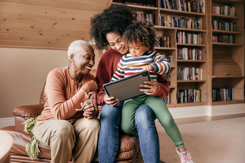 Three generations sit in an overstuffed chair looking at tablet.