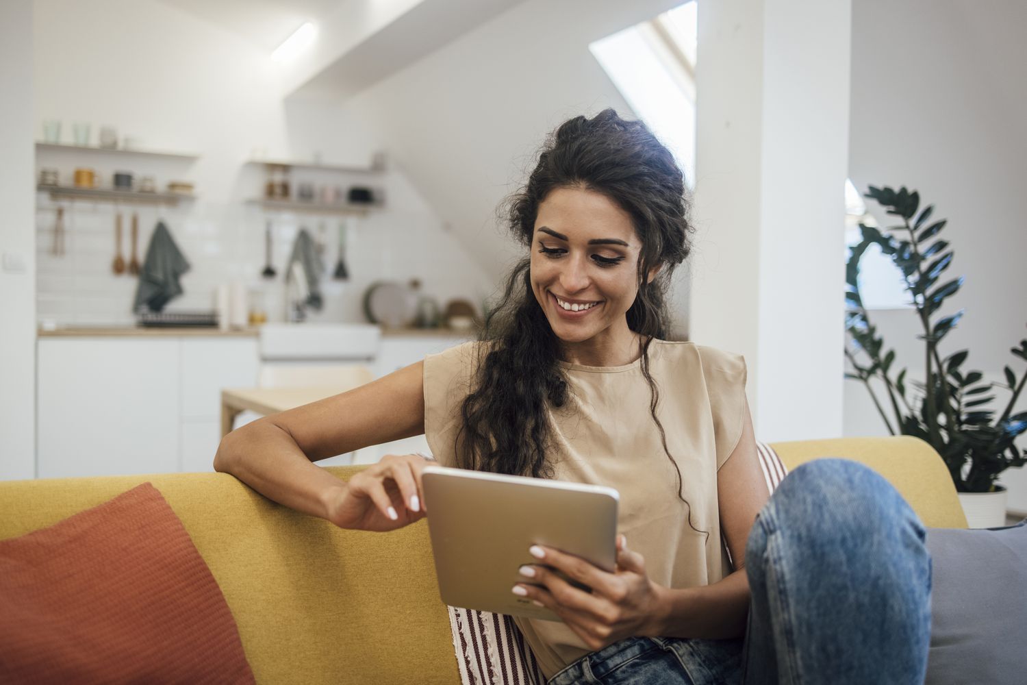 A happy young woman looks at a tablet while sitting on a couch; she's banking online.