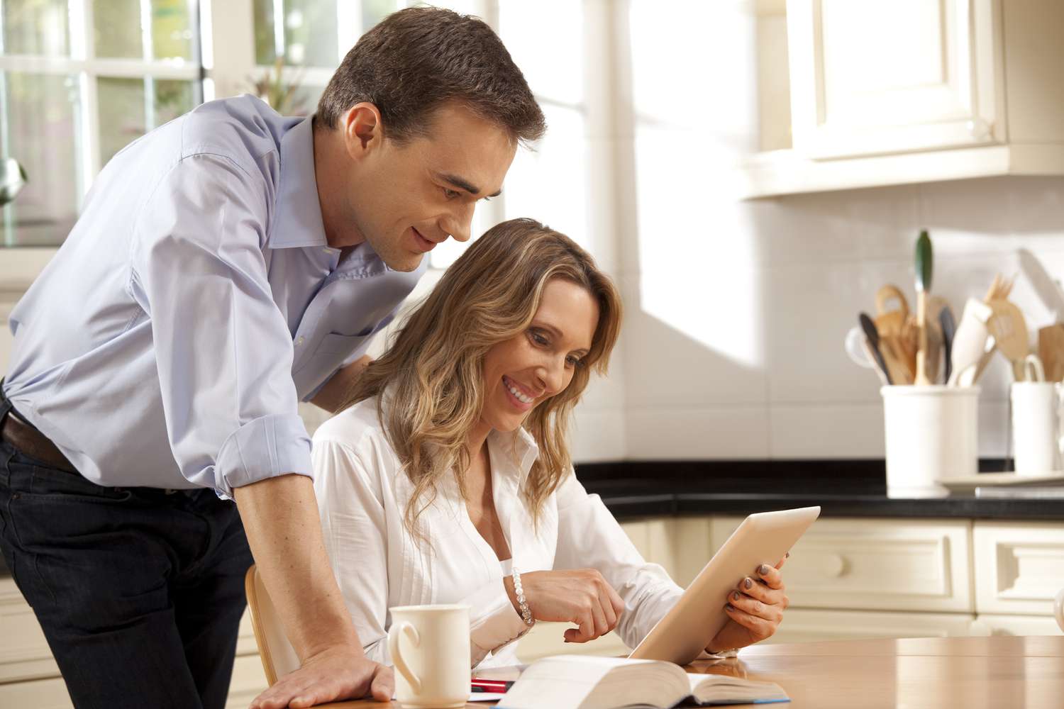 Couple in their 30s in their kitchen and looking happily at mortgage rates on a tablet