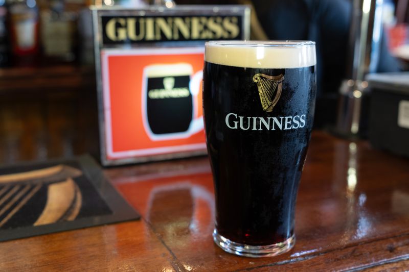 A pint glass full of Guinness beer sits on a bar.