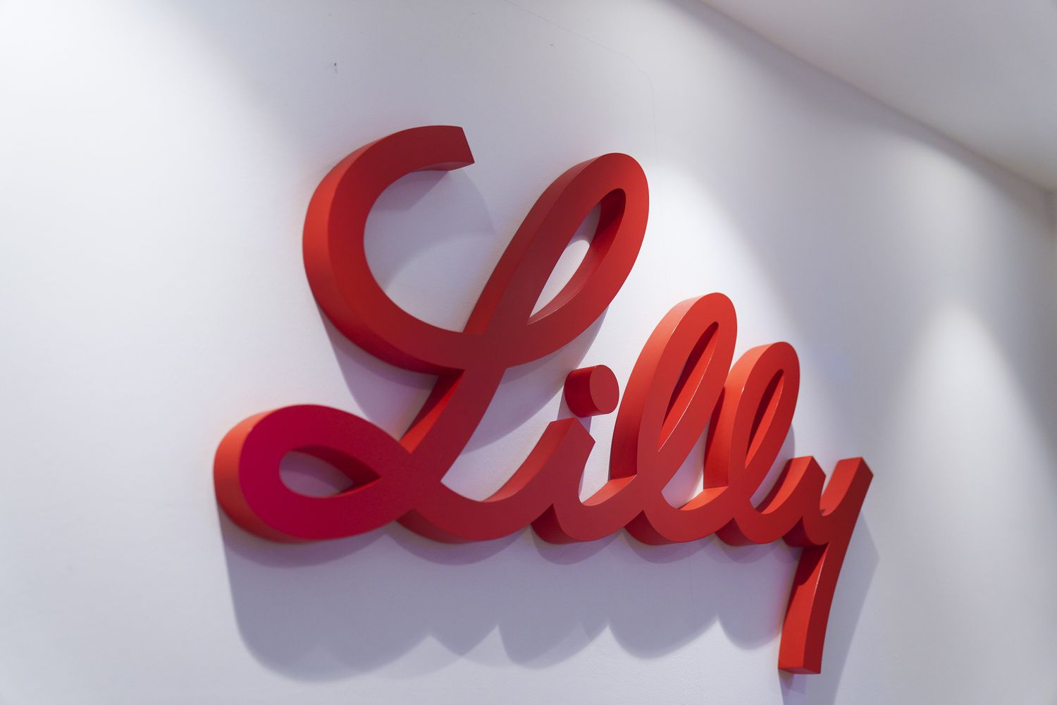 The red Lilly logo for Eli Lilly is seen on a white wall inside a building.