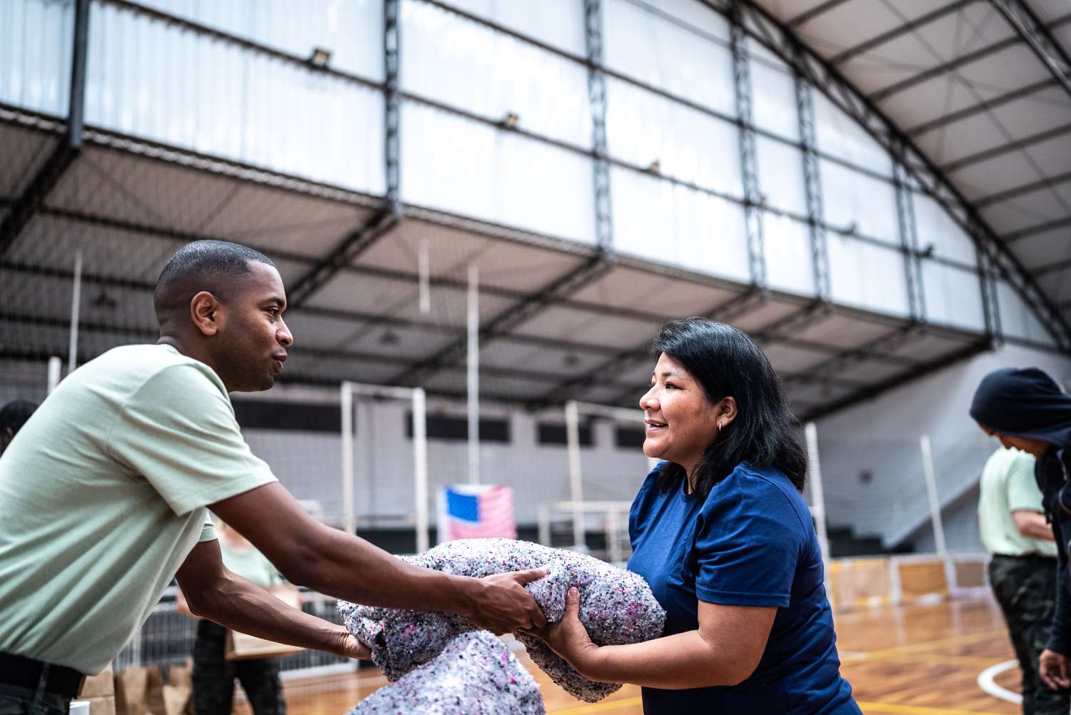 A soldier hands a woman a blanket in a gymnasium. 