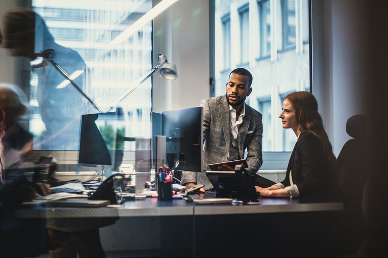 Two colleagues at an underwriting firm review information on a computer screen to determine how much risk an new initial public offering (IPO) will pose.