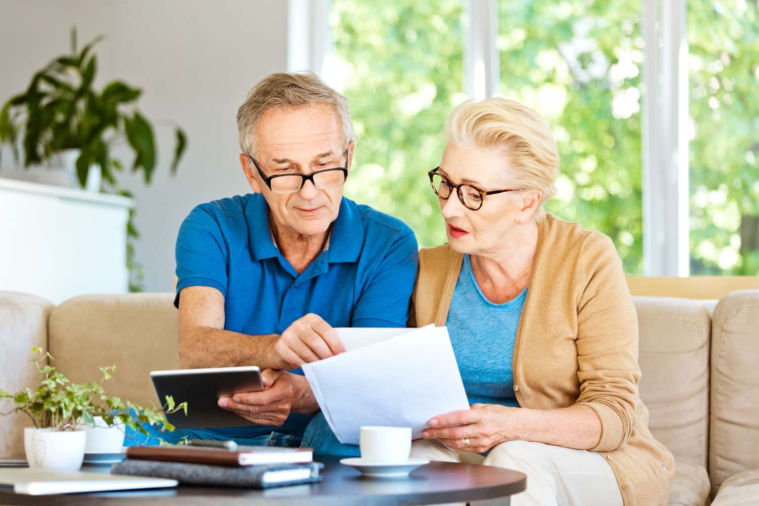 Older couple sitting on their sofa and looking together at bank statements and online rates.