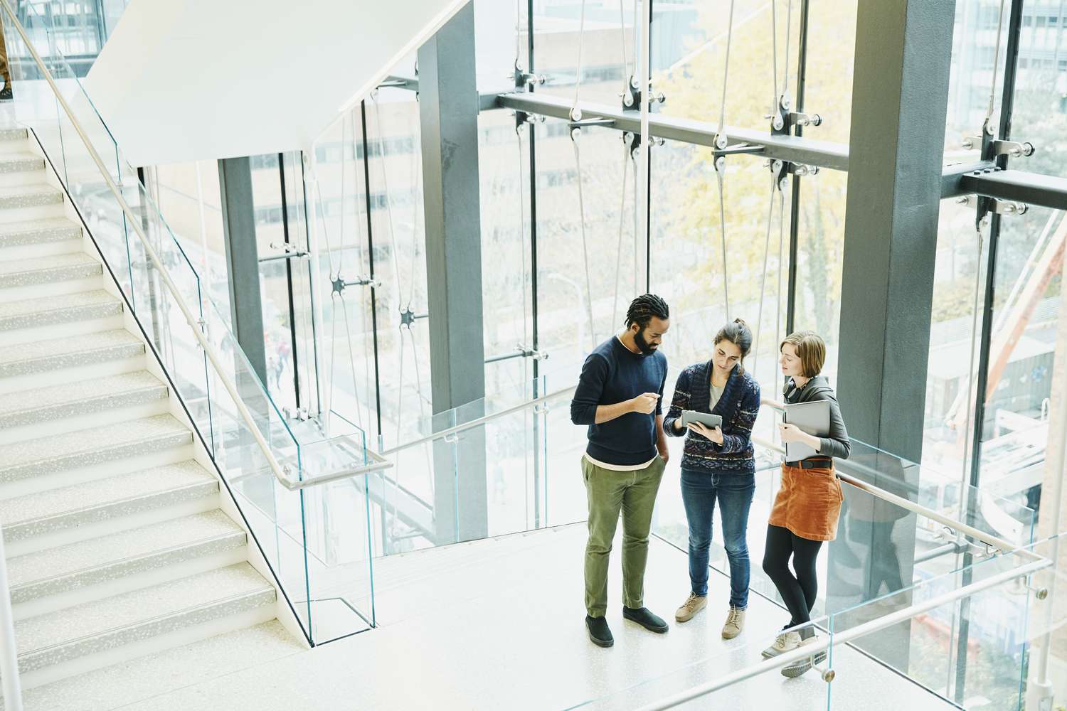 Coworkers discussing project on digital tablet on stairs of office building