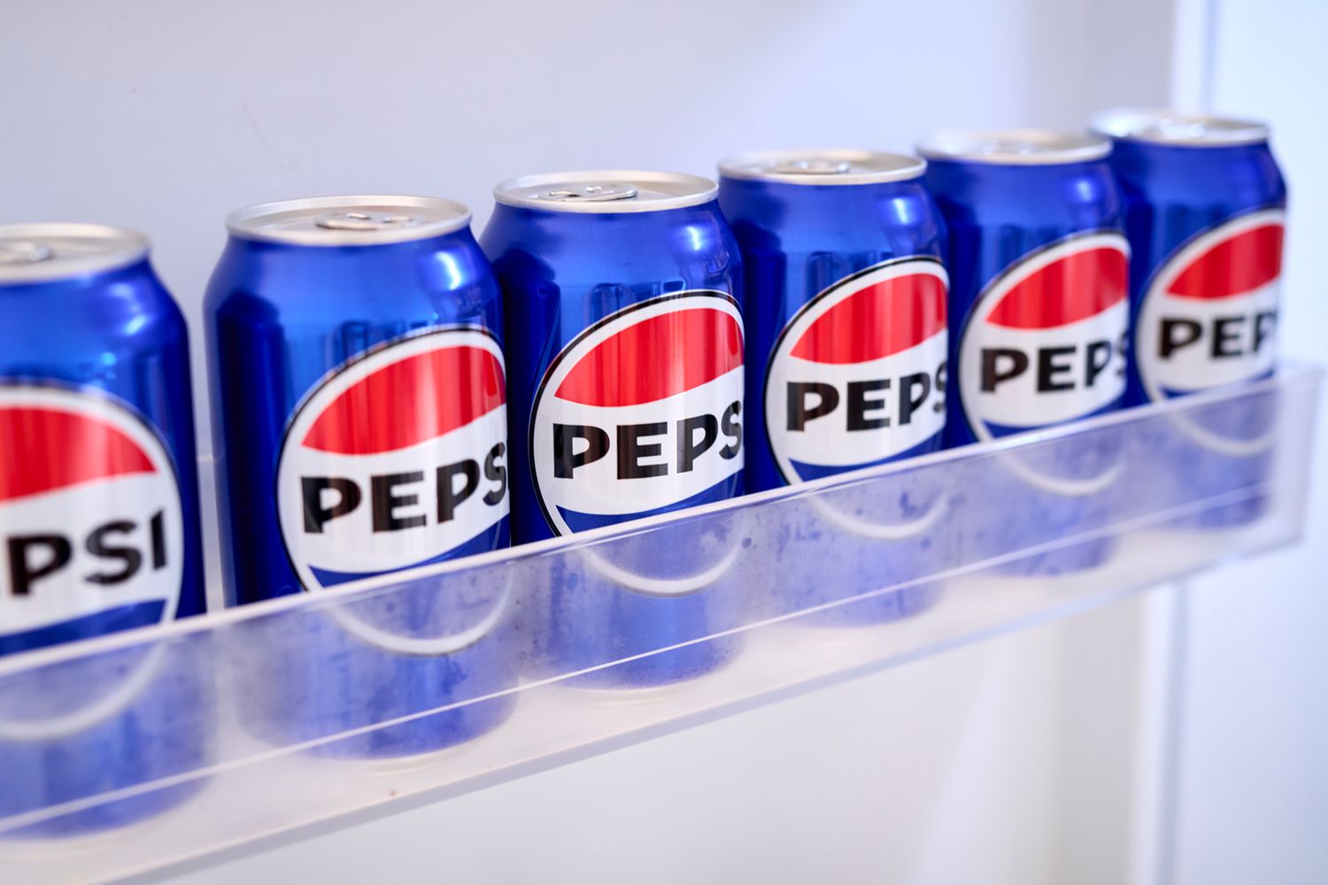 A row of blue Pepsi cans sit in a refrigerator shelf.
