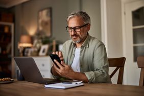 A man sitting at a desk uses a smart phone.