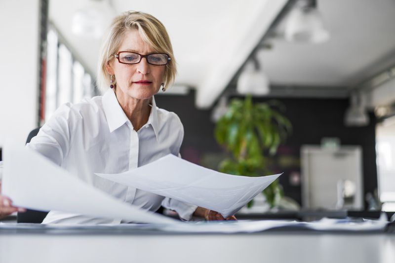 A business owner sits at their desk and shuffles through SEC paperwork to revoke their registration as a publicly-traded corporation.