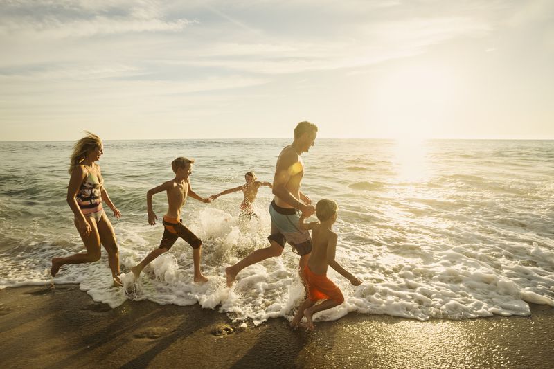 USA, California, Laguna Beach, Family with three children (6-7, 10-11, 14-15) running on beach
