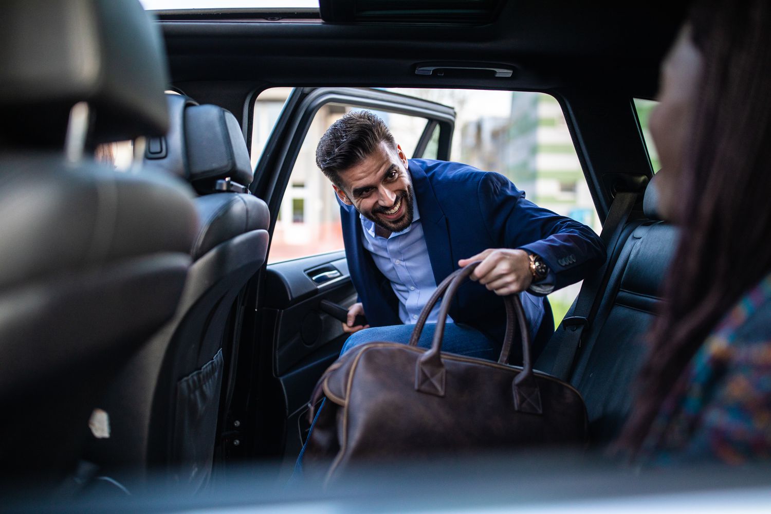 Businessman entering a car, holding luggage, his friends sitting in car and waiting for him