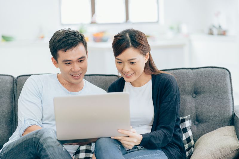 Young smiling couple sitting on their sofa and looking at mortgage rates on a laptop