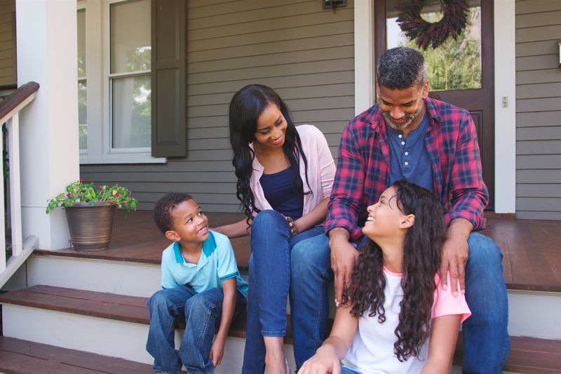Portrait Of Smiling Family Sitting On Steps Of Suburban Home