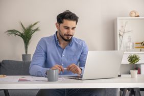 Young man sitting at his desk and looking seriously at his laptop 