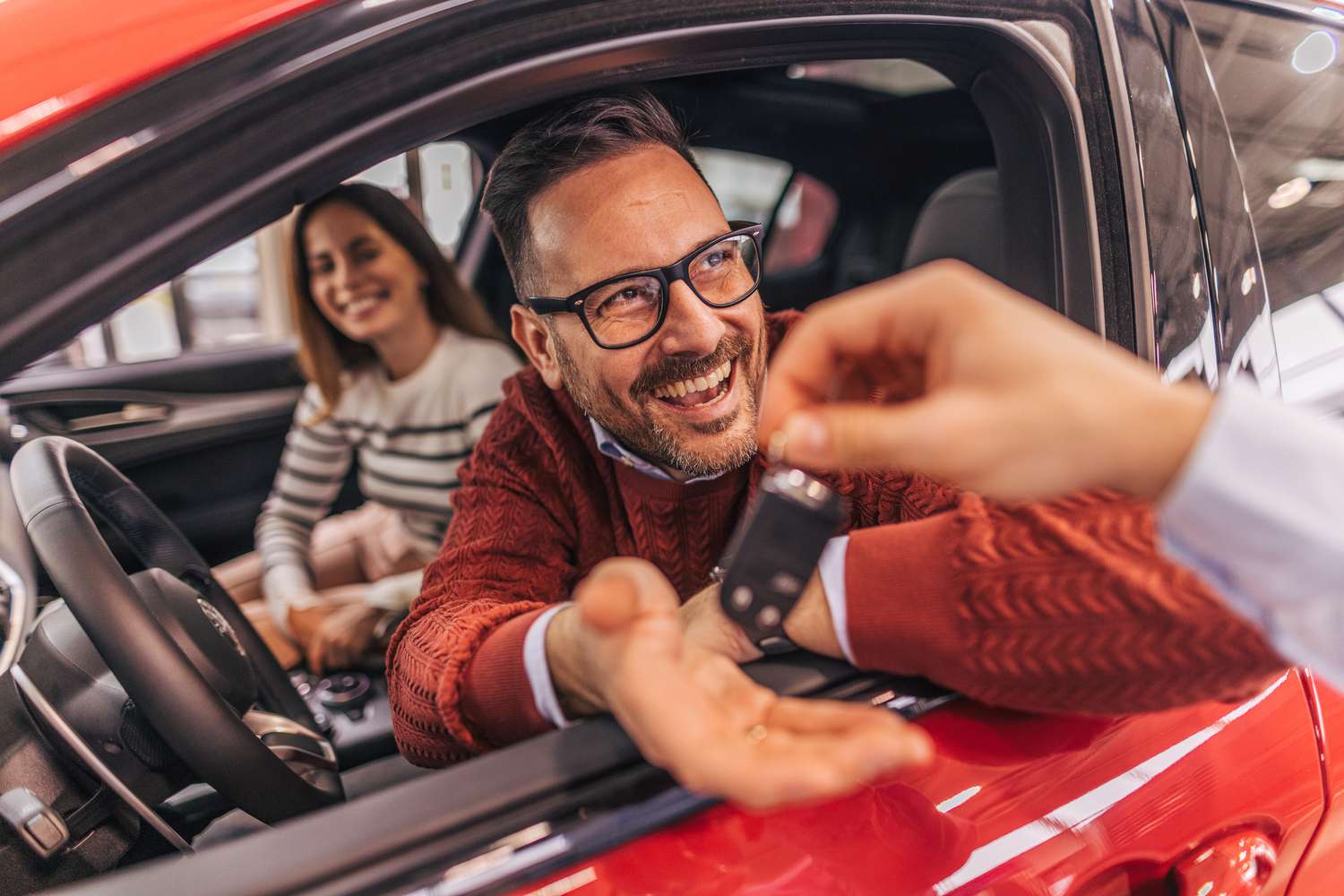 A couple sitting in a car, receiving the keys from a car dealer, both excited and happy to take ownership of their new vehicle