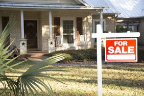 Stone house with a red "for sale" sign in front of it 