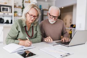Two older adults focused on paperwork and a laptop on a table