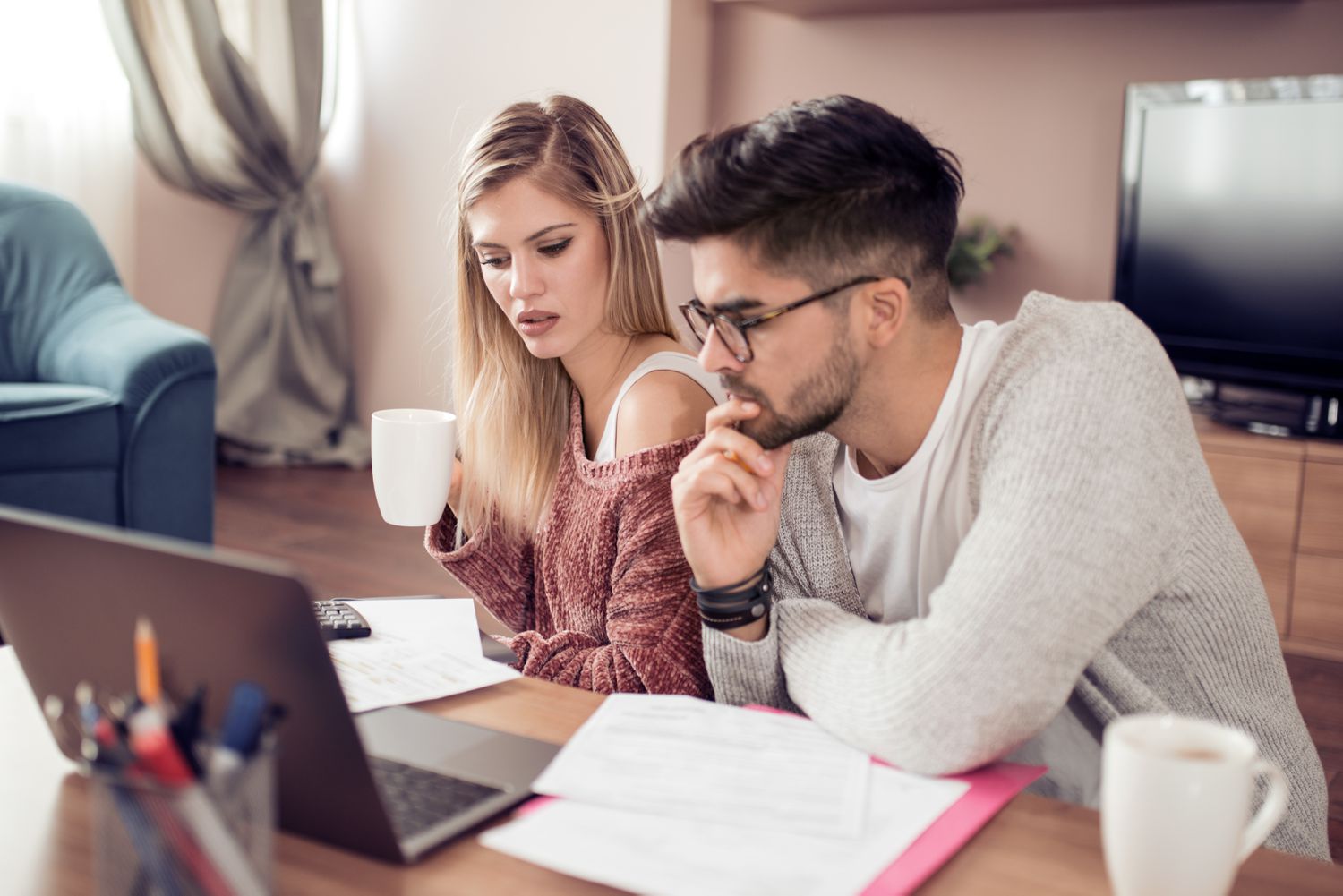 Young couple sitting in their living room and looking with concern at documents and a laptop