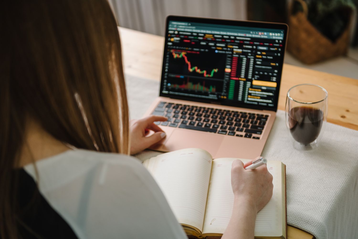 Woman looking at a candlestick chart on her laptop and making notes on a pad