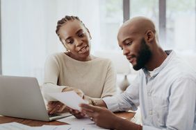 Couple looking at papers and laptop discussing whether to change their mortgage company.