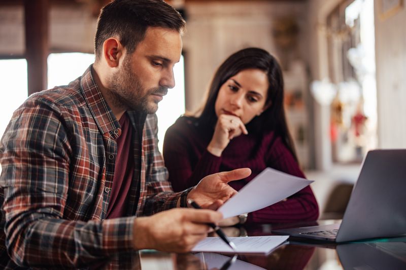 A couple filing form 4684 for tax deduction together in their living room in front of their laptop.