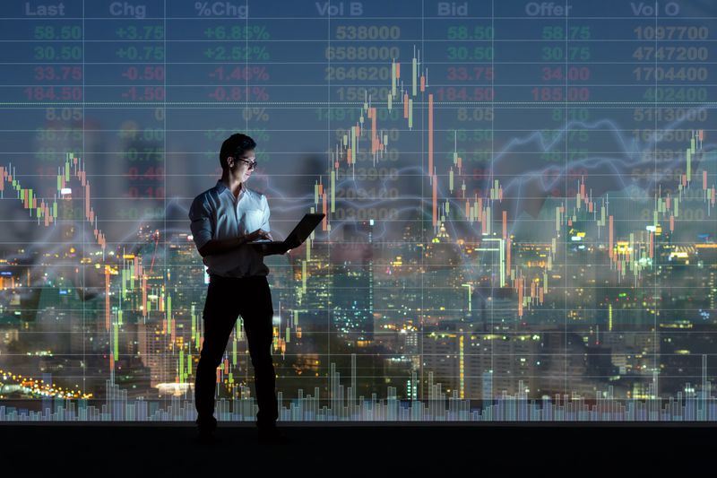 a man holding a laptop in front of a skyline overlaid with a line graph and bid offer numbers