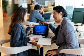 An investment advisor and client talk with a small laptop between them.