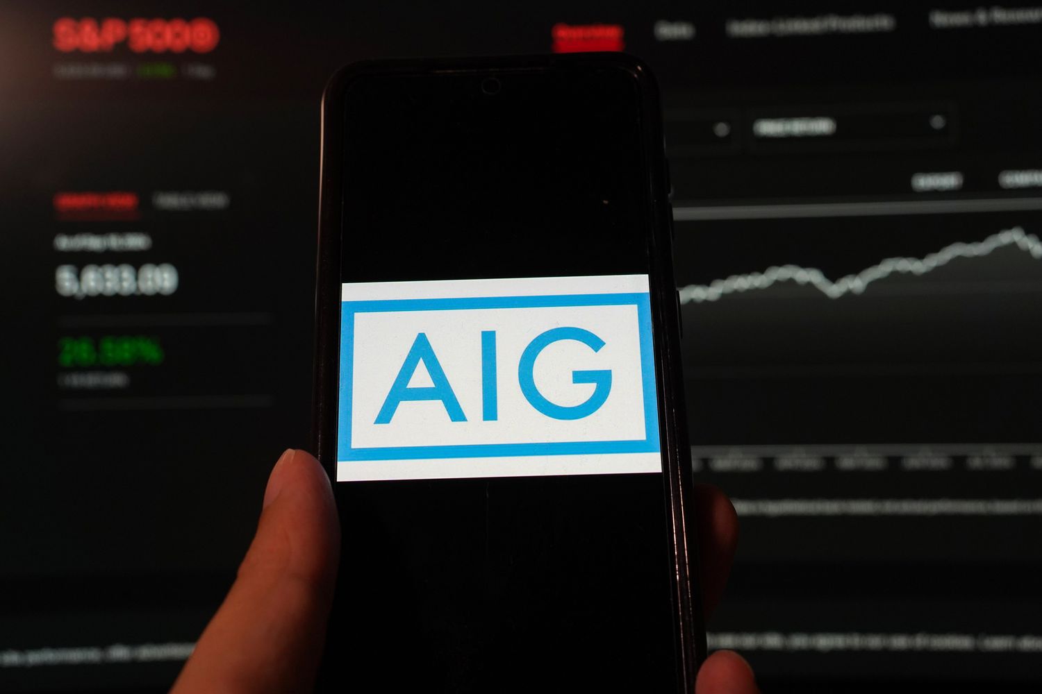 American International Group (AIG) logo is displayed on a smartphone with a S&P index website background