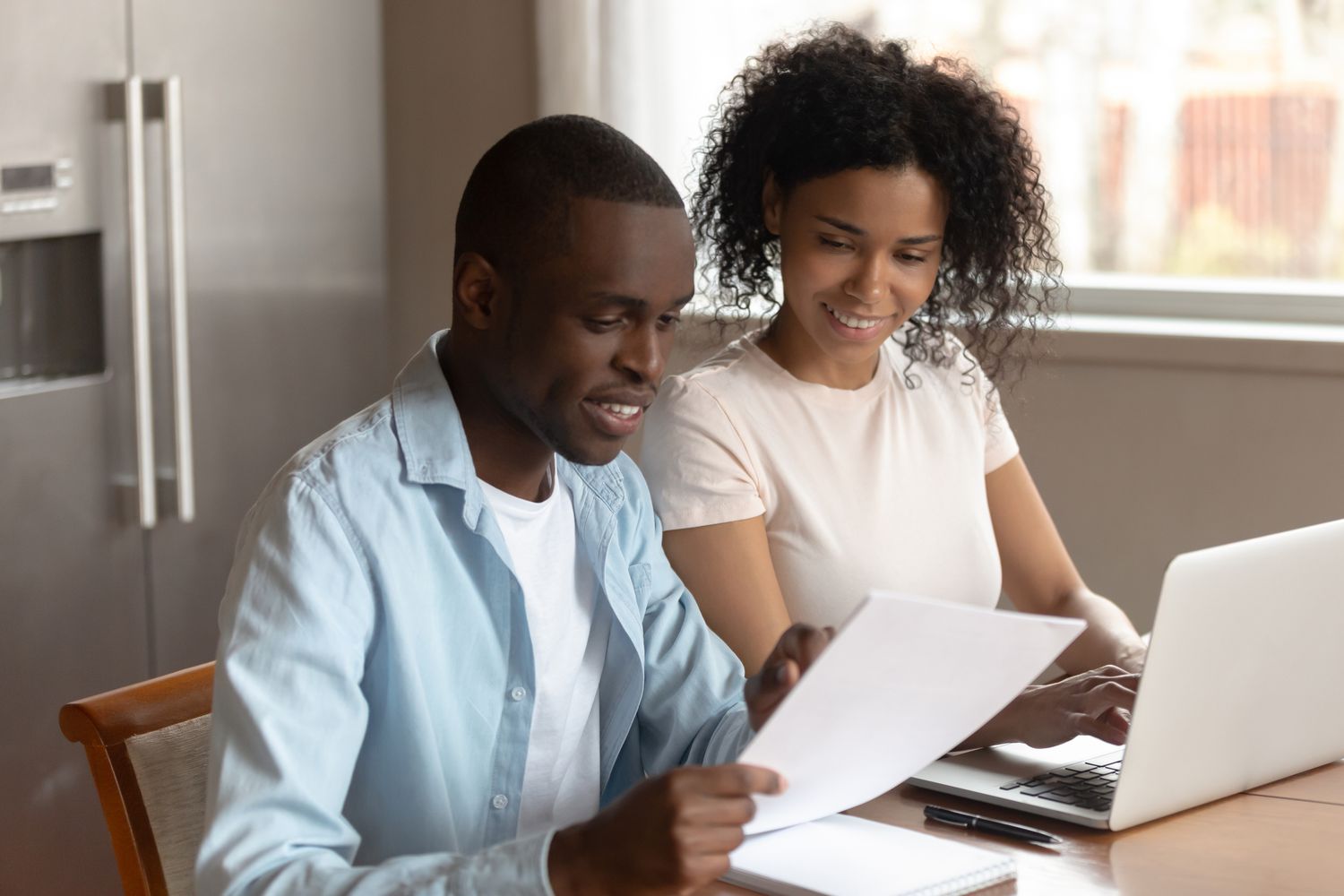 Young couple sitting in their kitchen and looking at mortgage documents and online rates