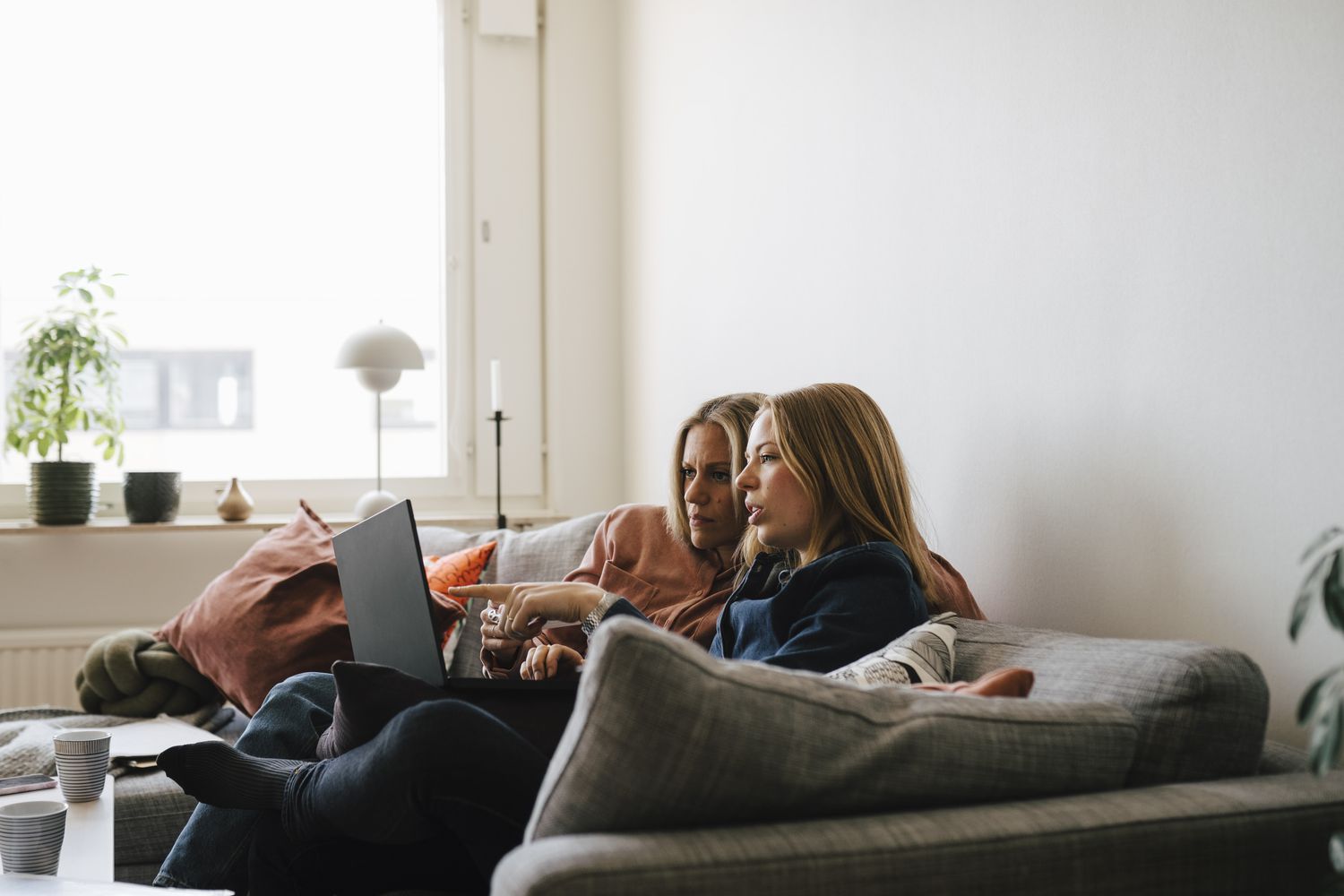 Two women sit on a couch looking at a laptop