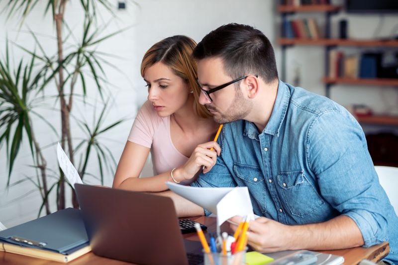 Young couple sitting at home and looking seriously at mortgage documents, a calculator, and a laptop