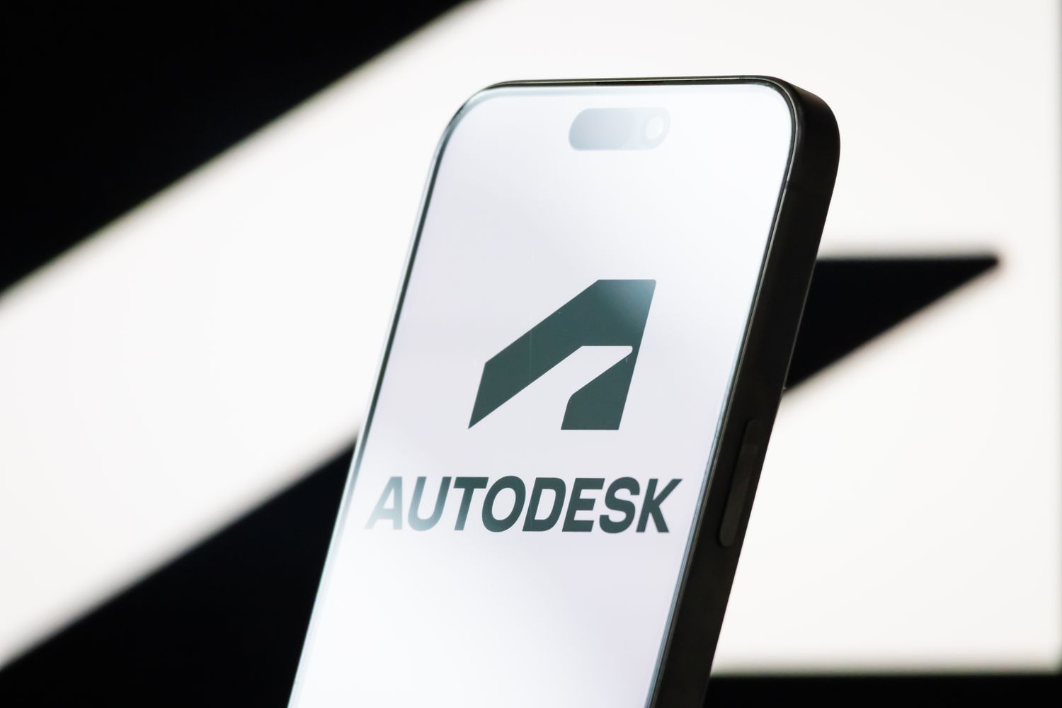 The logo of Autodesk, Inc. is displayed on a smartphone screen, with the company's bold black-and-white branding in the background