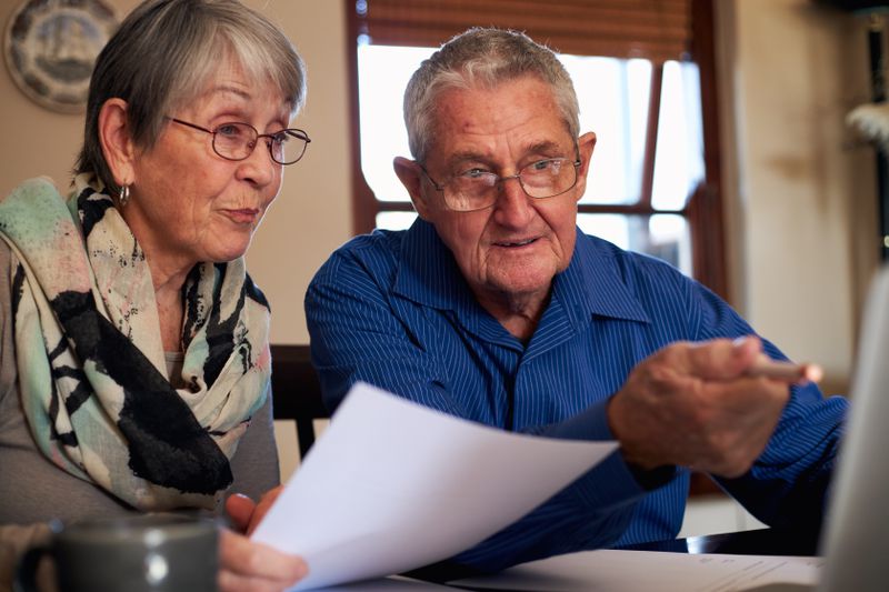 Older couple sitting at their dining room table and looking at mortgage documents and a laptop