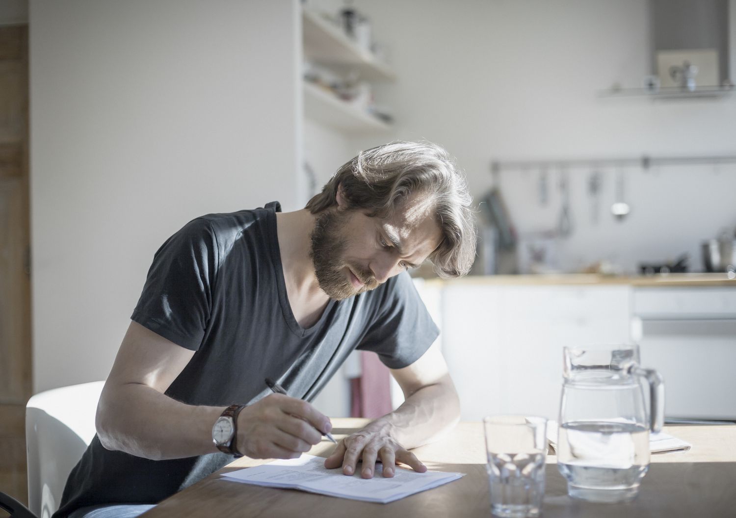 Man in casual clothing sitting at home writing on papers on the kitchen table