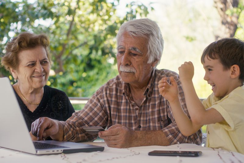 A young child celebrates as their grandparents use a laptop to show them the value of their savings bonds account.