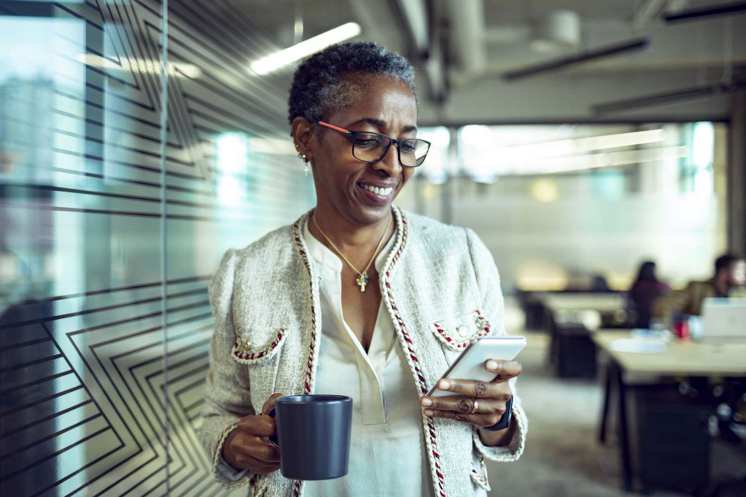 An older employee holds coffee and checks her phone.